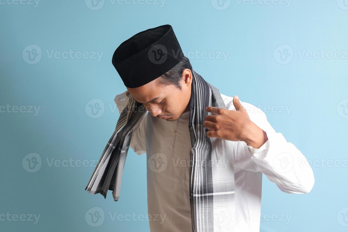 Portrait of Asian muslim man in white koko shirt folding and tidy up his sarung . Isolated image on blue background photo
