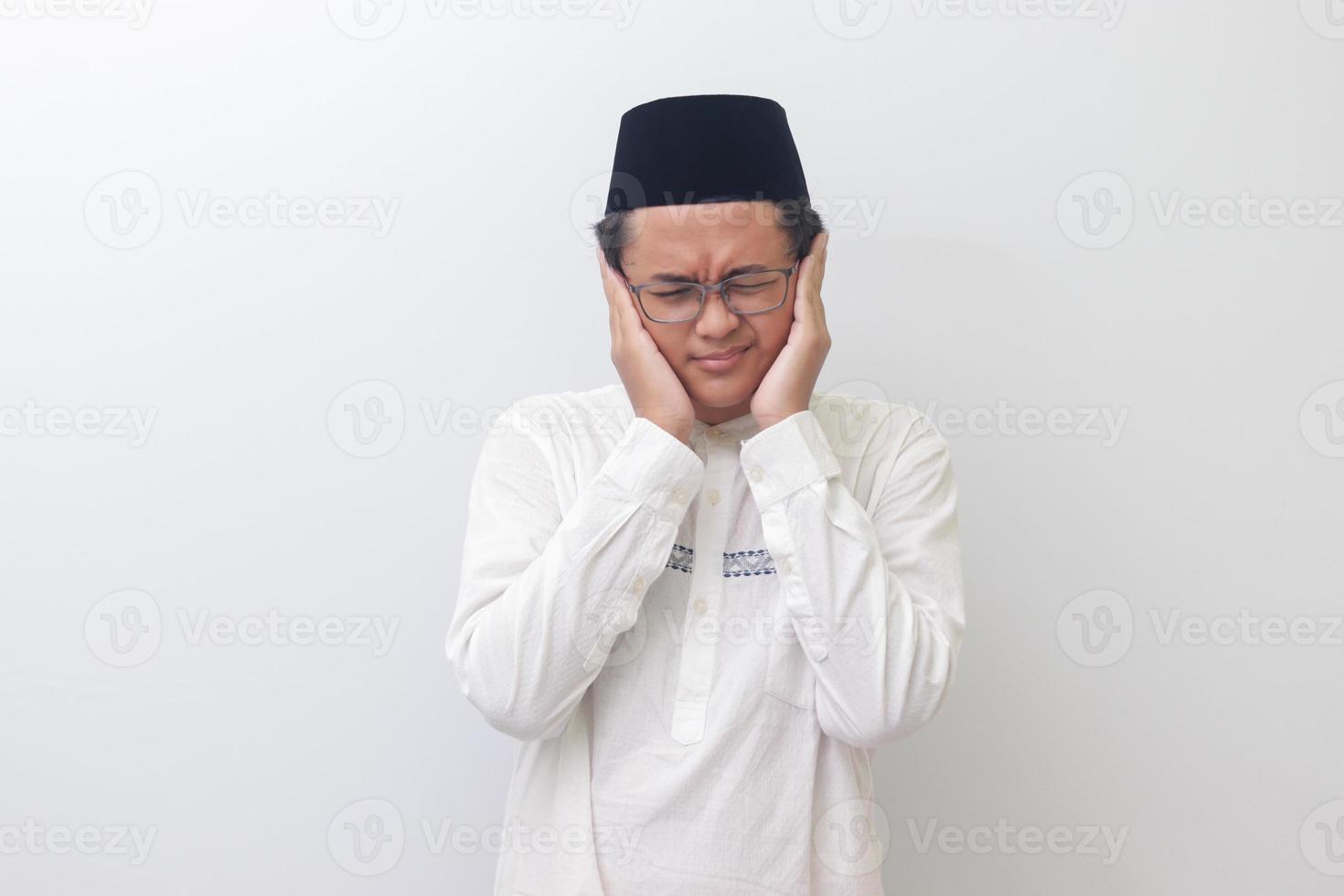 Portrait of young Asian muslim man covering ears with fingers with annoyed expression for the noise of loud music and sound. Isolated image on white background photo