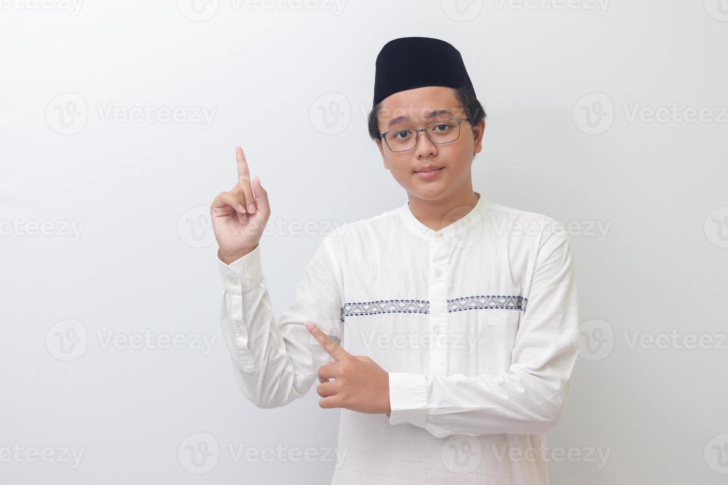 Portrait of young Asian muslim man showing product and pointing with his hand and finger. Isolated image on white background photo