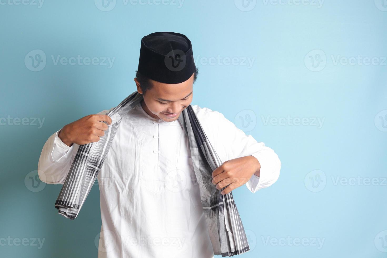 retrato de asiático musulmán hombre en blanco koko camisa plegable y ordenado arriba su Sarung . aislado imagen en azul antecedentes foto