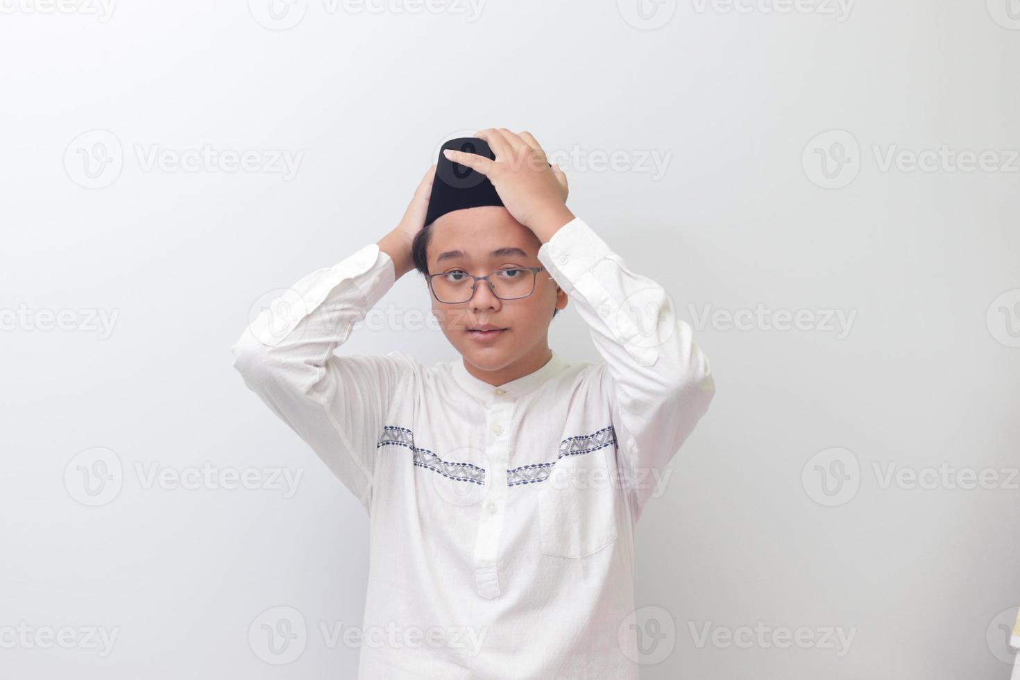 Portrait of young Asian muslim man trying to adjust his songkok or black skullcap. Isolated image on white background photo