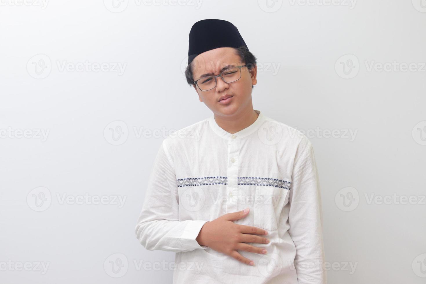 Portrait of young Asian muslim man feeling pain in his stomach. Stomachache concept. Isolated image on white background photo