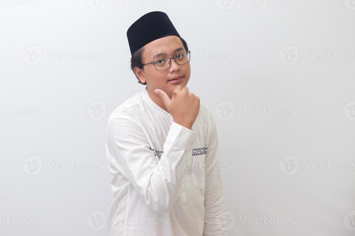 Portrait of young Asian muslim man smiling and looking at camera, making thumbs up hand gesture. Isolated image on white background photo