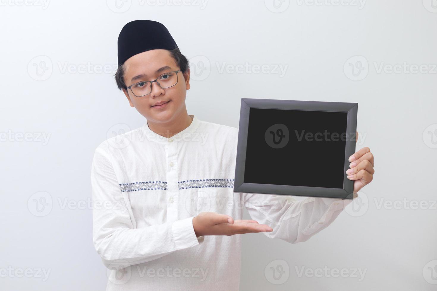 Portrait of young Asian muslim man holding a blackboard with hand pointed. Blank space for typography or text to fill. Isolated image on white background photo