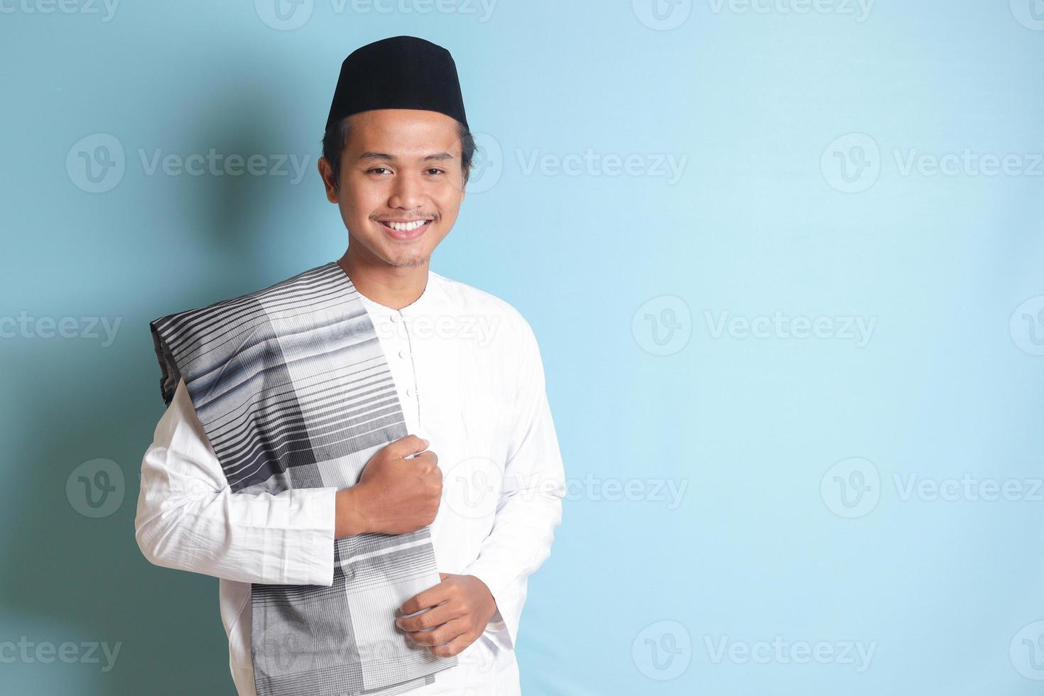 Portrait of Asian muslim man in white koko shirt feeling confident, smiling and looking at camera. Isolated in blue background photo