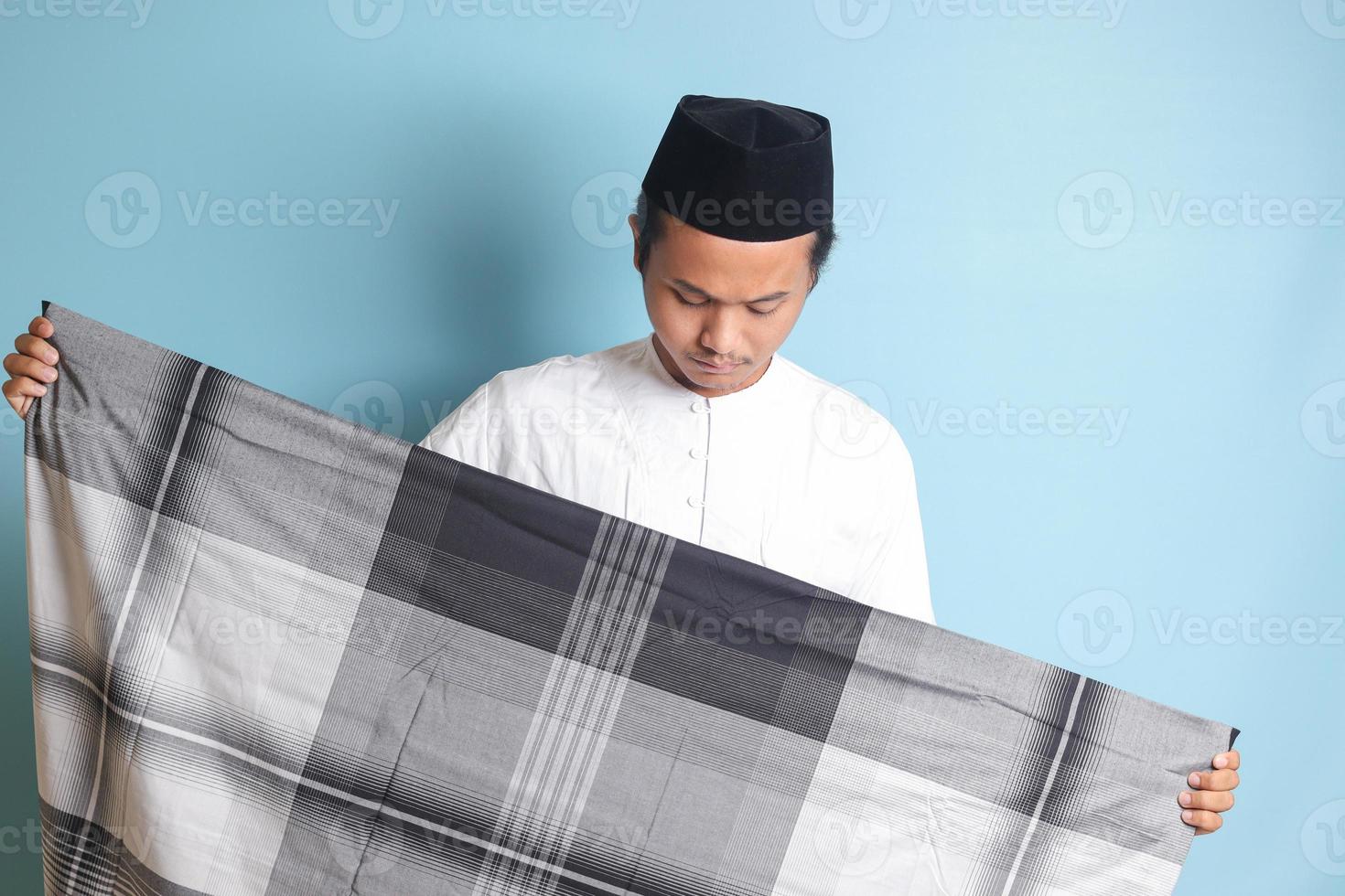 retrato de asiático musulmán hombre en blanco koko camisa plegable y ordenado arriba su Sarung . aislado imagen en azul antecedentes foto