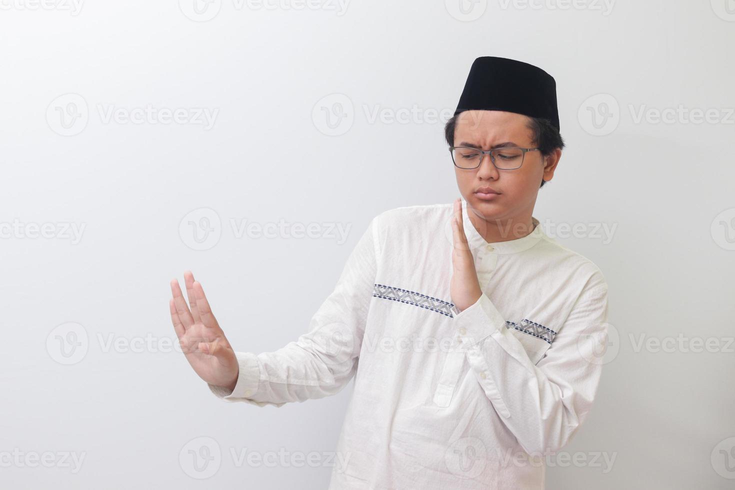 Portrait of young Asian muslim man forming a hand gesture to avoid something or bad things. Isolated image on white background photo