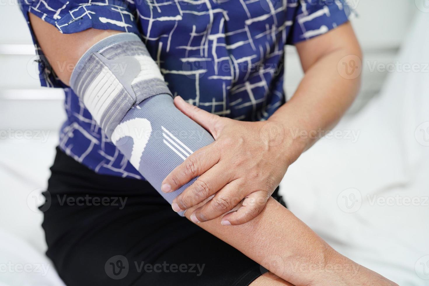 Asian senior woman wearing elastic support elbow brace for reduce pain. photo