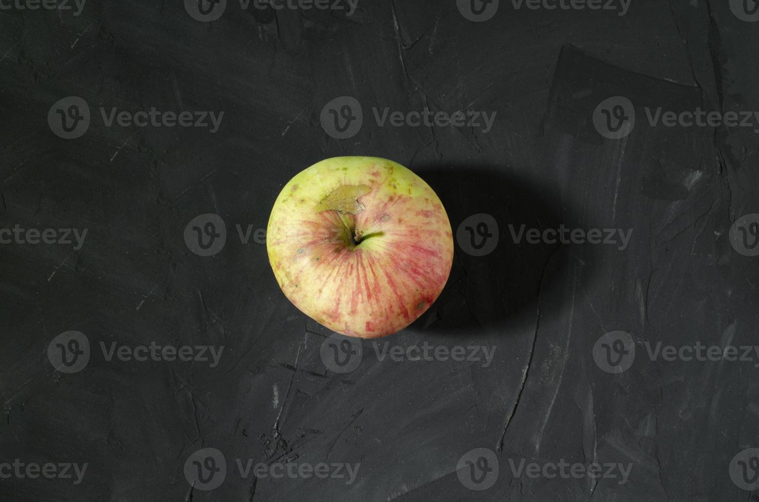 The single apple in the middle of the dark gray background. Red and yellow ripe apple. Concrete background. photo