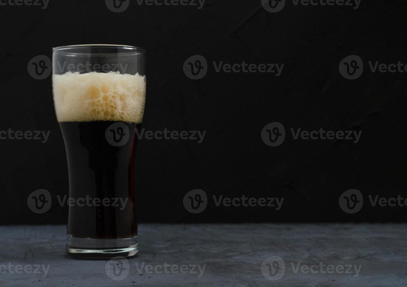 A pint of dark beer with foam, Dark background. photo