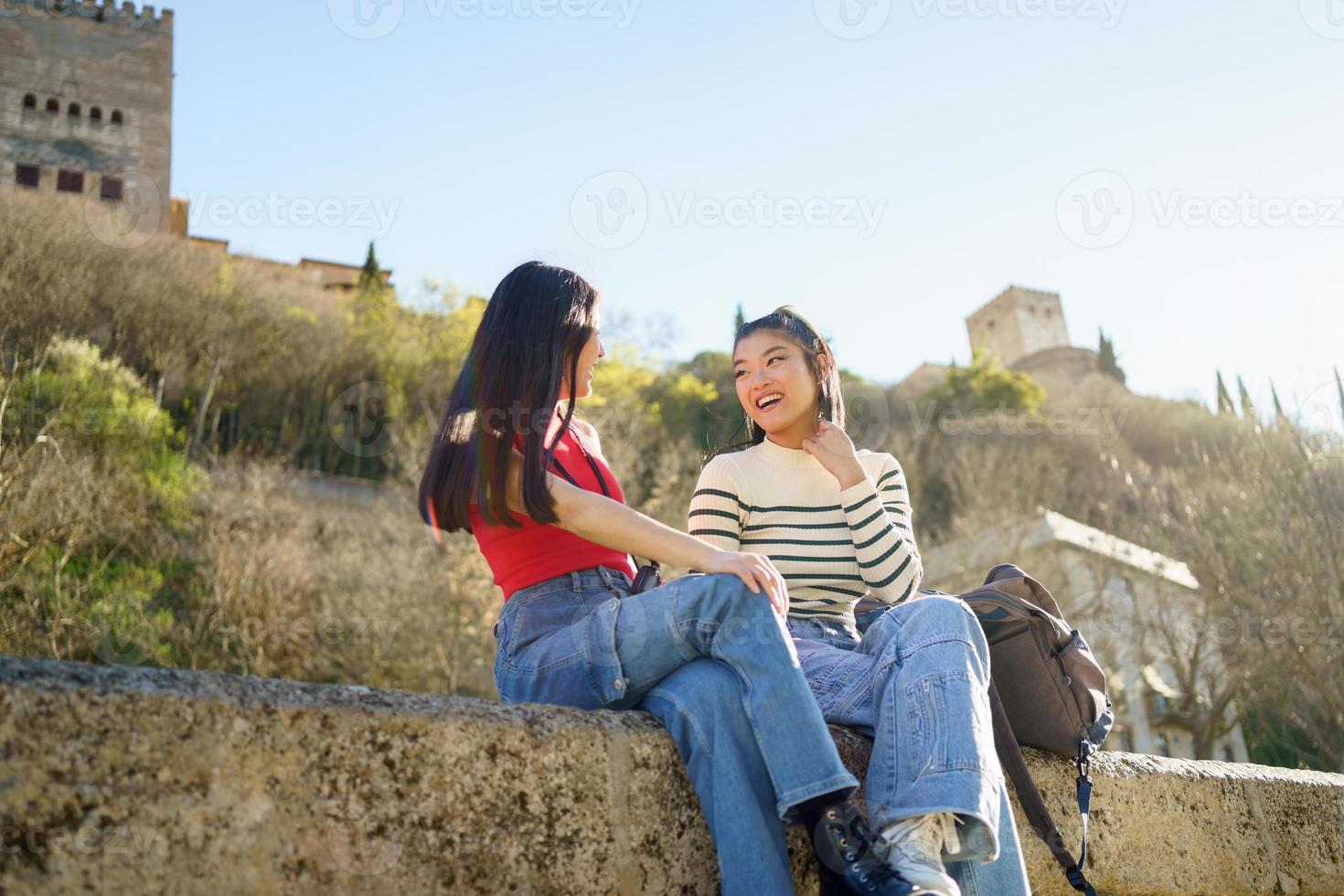 Cheerful Asian women sitting on stone border and smiling photo