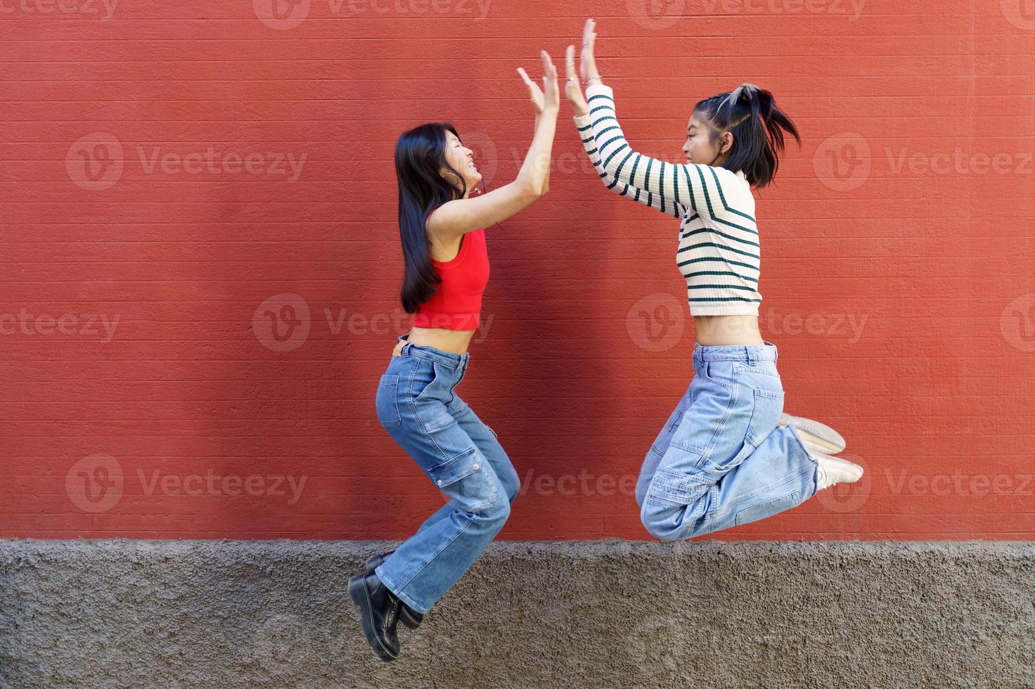 Joyful young Asian girlfriends giving high five while jumping photo