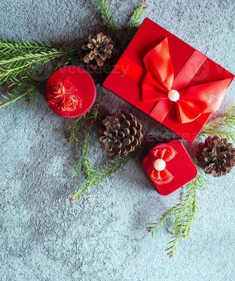 Christmas decoration composition on gray concrete background with a beautiful Red gift box with red ribbon, tree branches, and pine cones photo