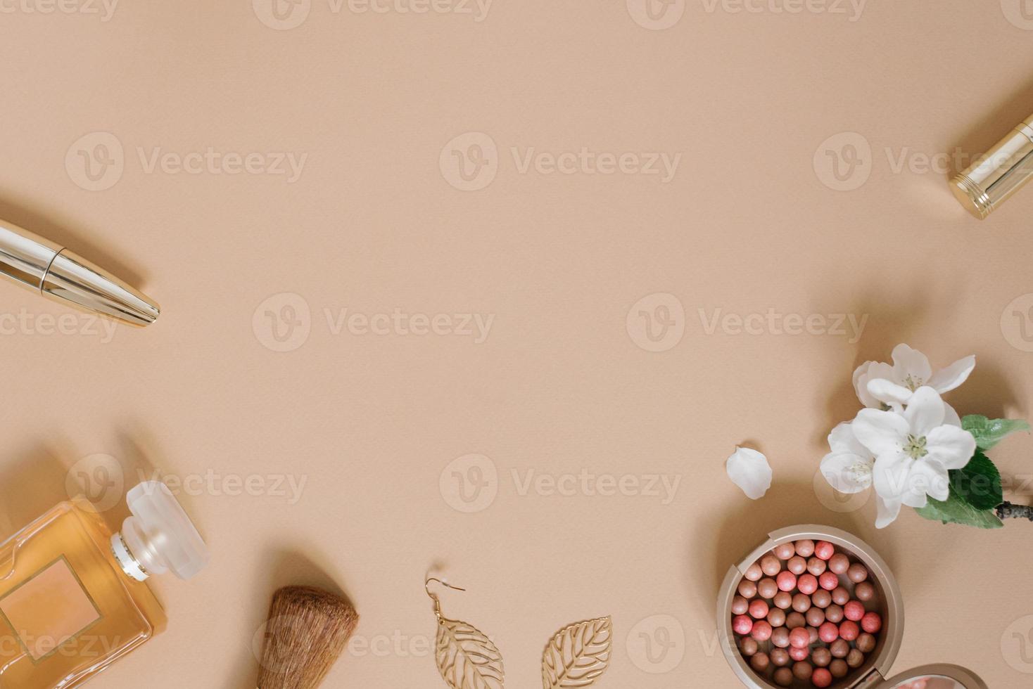 Frame with a set of makeup cosmetics, flowers and other accessories on a beige background. Composition in gold tones. Flat lay, top view. photo