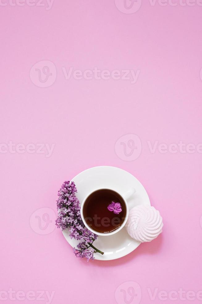 A white cup with coffee and marshmallows and beautiful lilac flowers on a pink background. Top view, flat, lying, copy space. photo