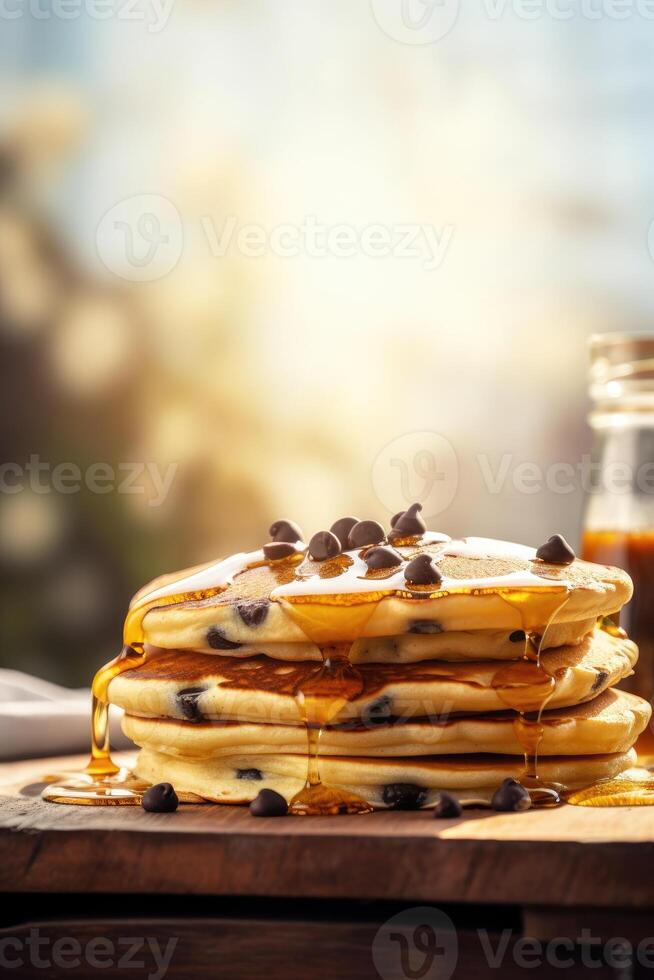 Syrup is poured down and chocolate chips are on top tall stack of golden pancakes layered on a plate with melted butter and syrup dripping down the sides of the stack. . photo