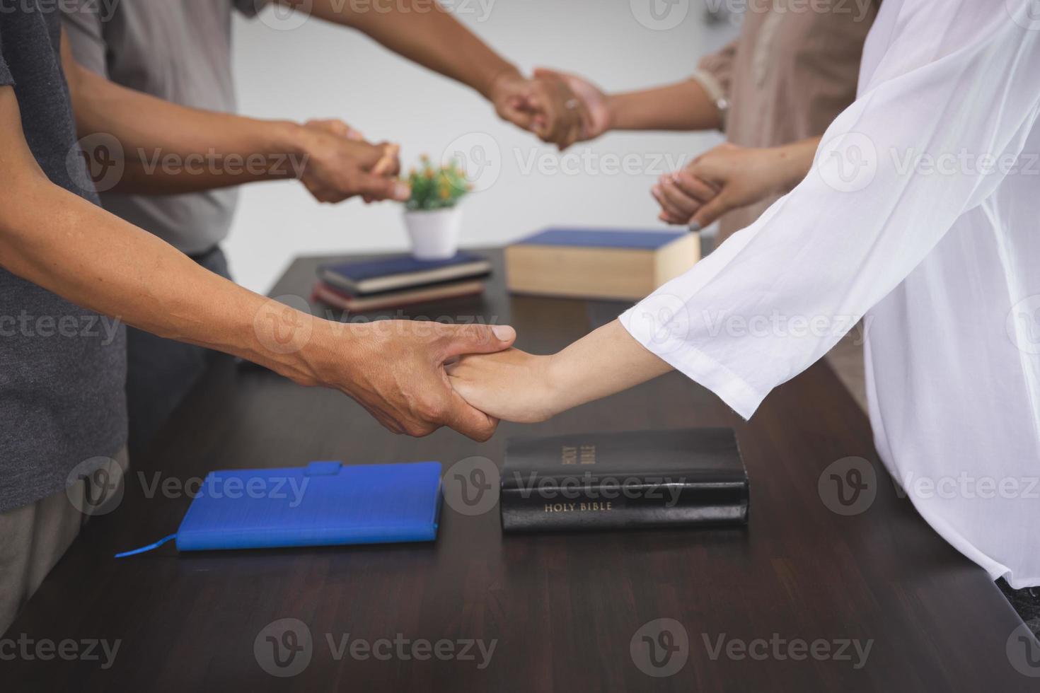 group of people holding hands in remembrance of god On the table there is a Bible, Respect, Spirituality and Religion. Christian background education Searching or studying the Bible. photo