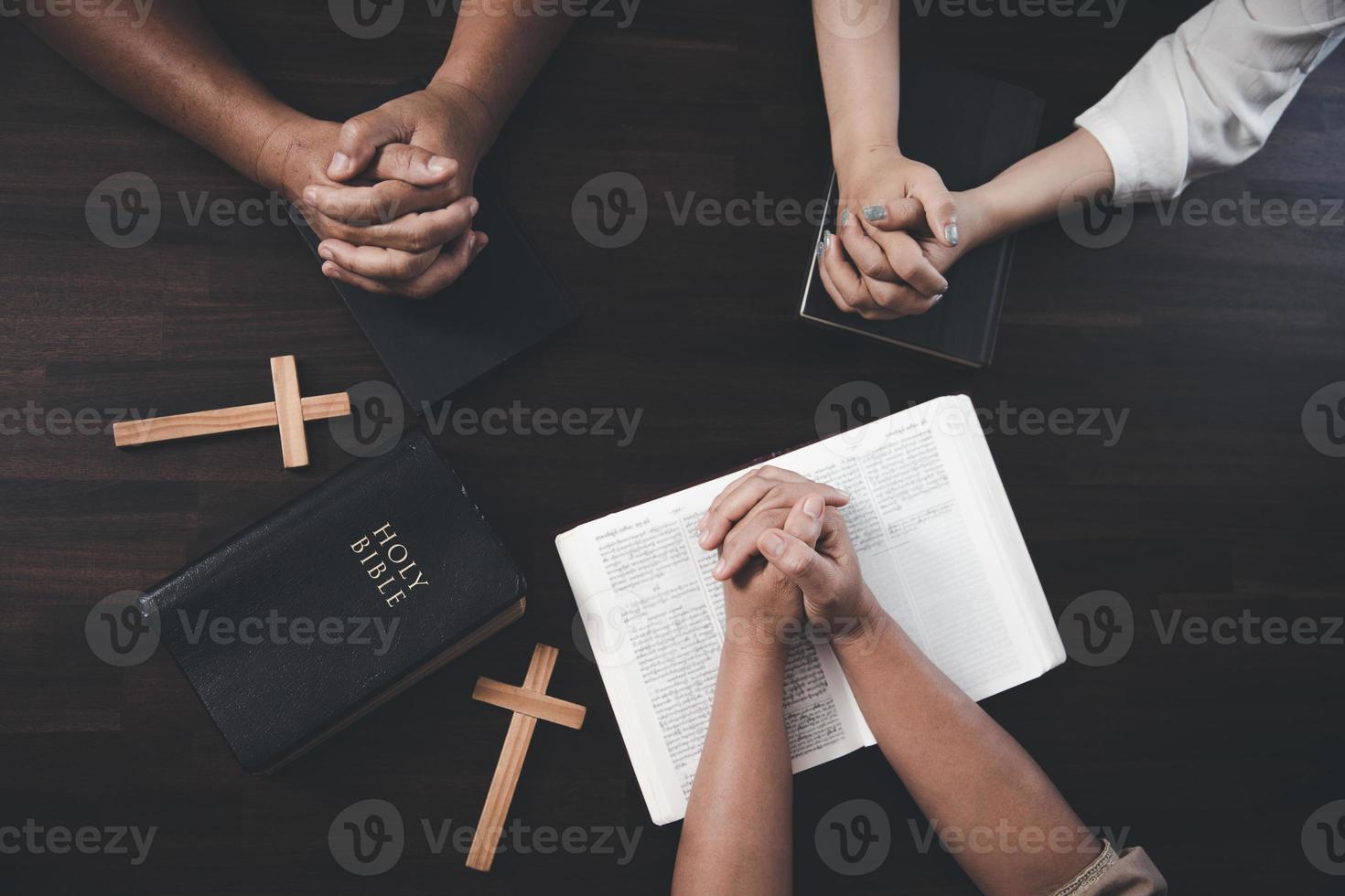 Small groups of Christians hold hands and pray together around a wooden table with bible pages and crosses. bible study group Learning religious concepts in the Bible. Worship God. photo