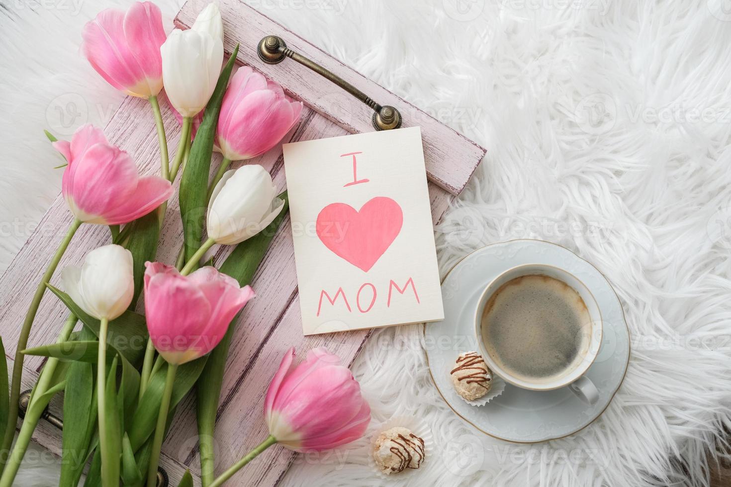 A bouquet of tulips, a cup of coffee and a card with the text I love mom on a tray. Mother's day concept photo