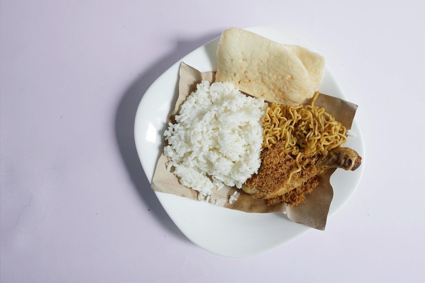 Padang cuisine, White rice with chicken and fried noodles on a white plate on a plain background photo