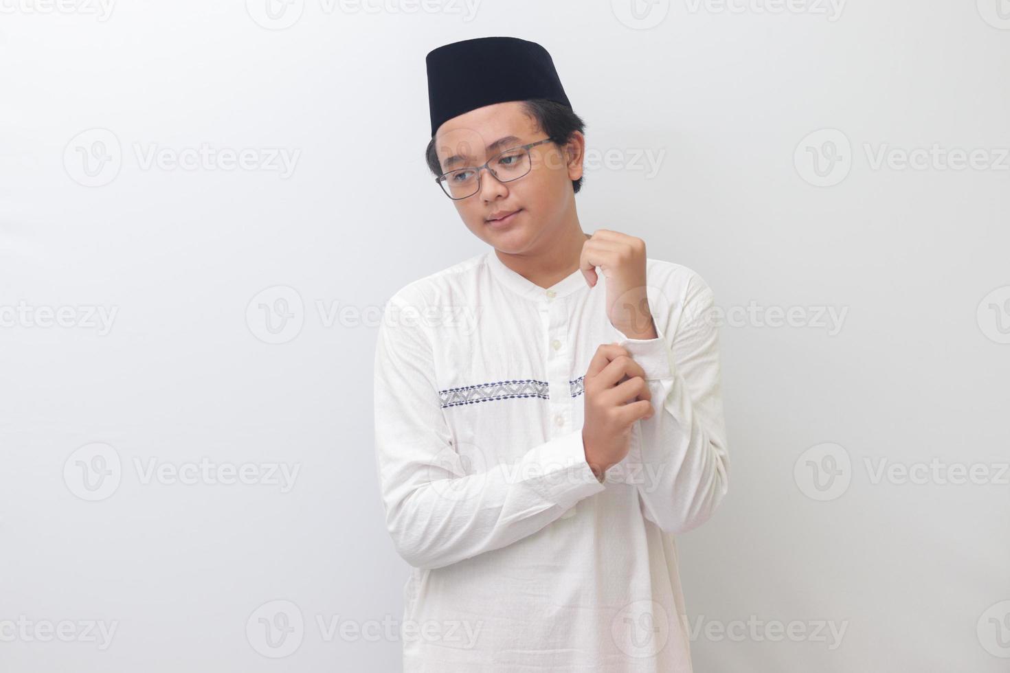 Portrait of young Asian muslim man trying to fix his shirt buttons. Isolated image on white background photo