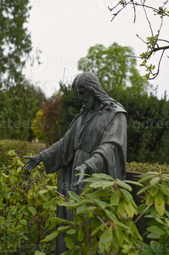 Old overgrown stone Jesus statue with bird drippings on its head photo