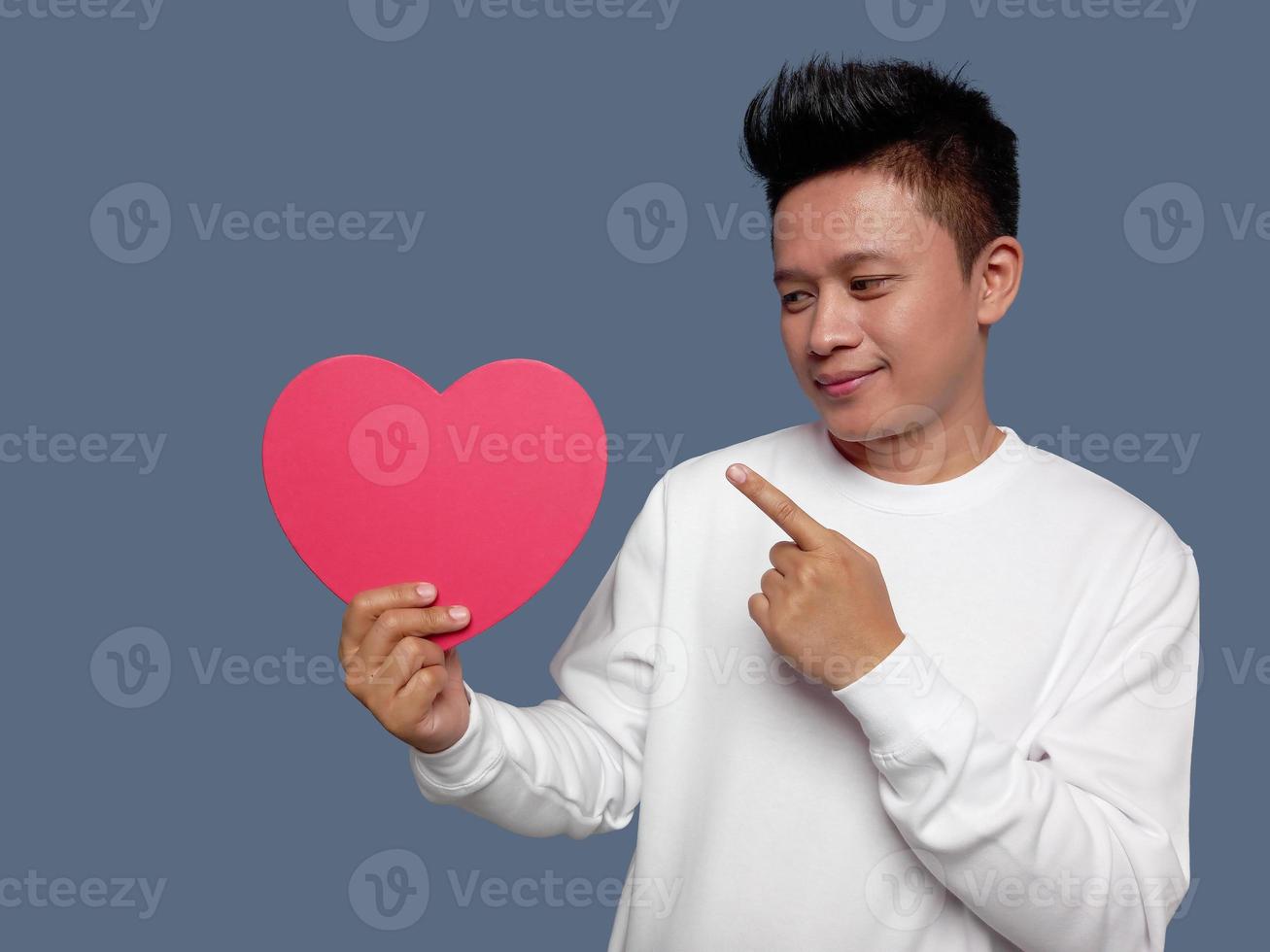 Man holding and pointing red heart shape isolated on plain background. photo
