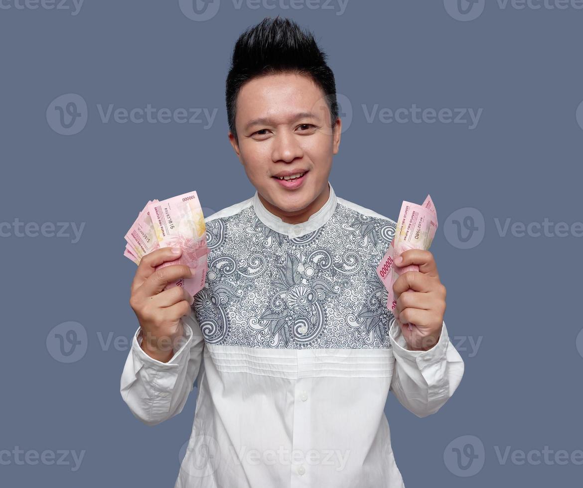 Young man wearing koko shirt holding one hundred thousand Indonesian rupiah in both hands photo