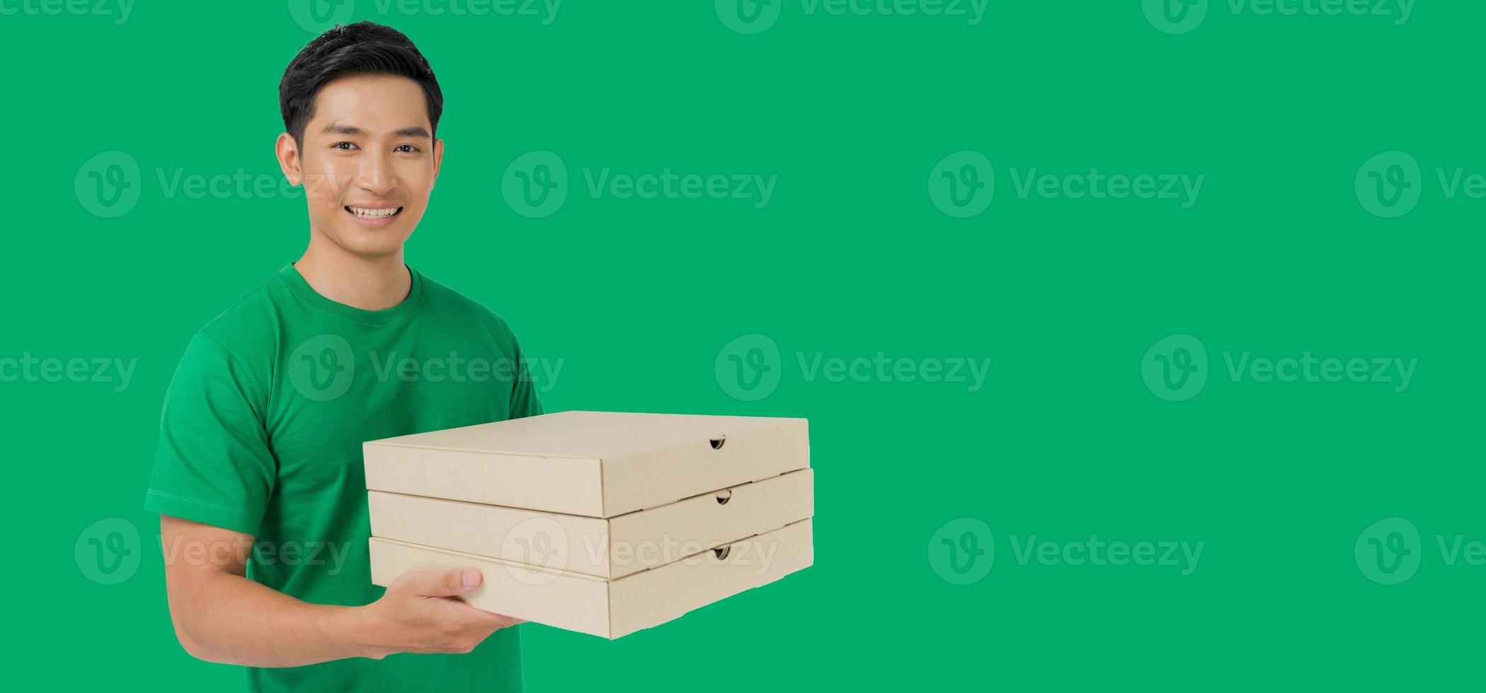 The smiling pizza delivery man stands on a green background holding the pizza box and wearing a green t-shirt uniform. photo