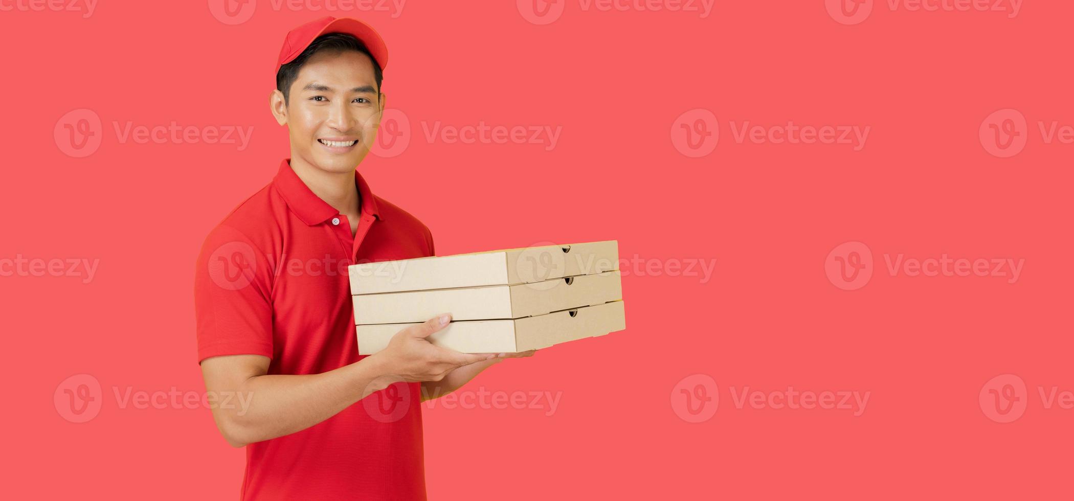 el sonriente Pizza entrega hombre soportes en un rojo antecedentes participación el Pizza caja y vistiendo un rojo gorra y un blanco camiseta uniforme. foto