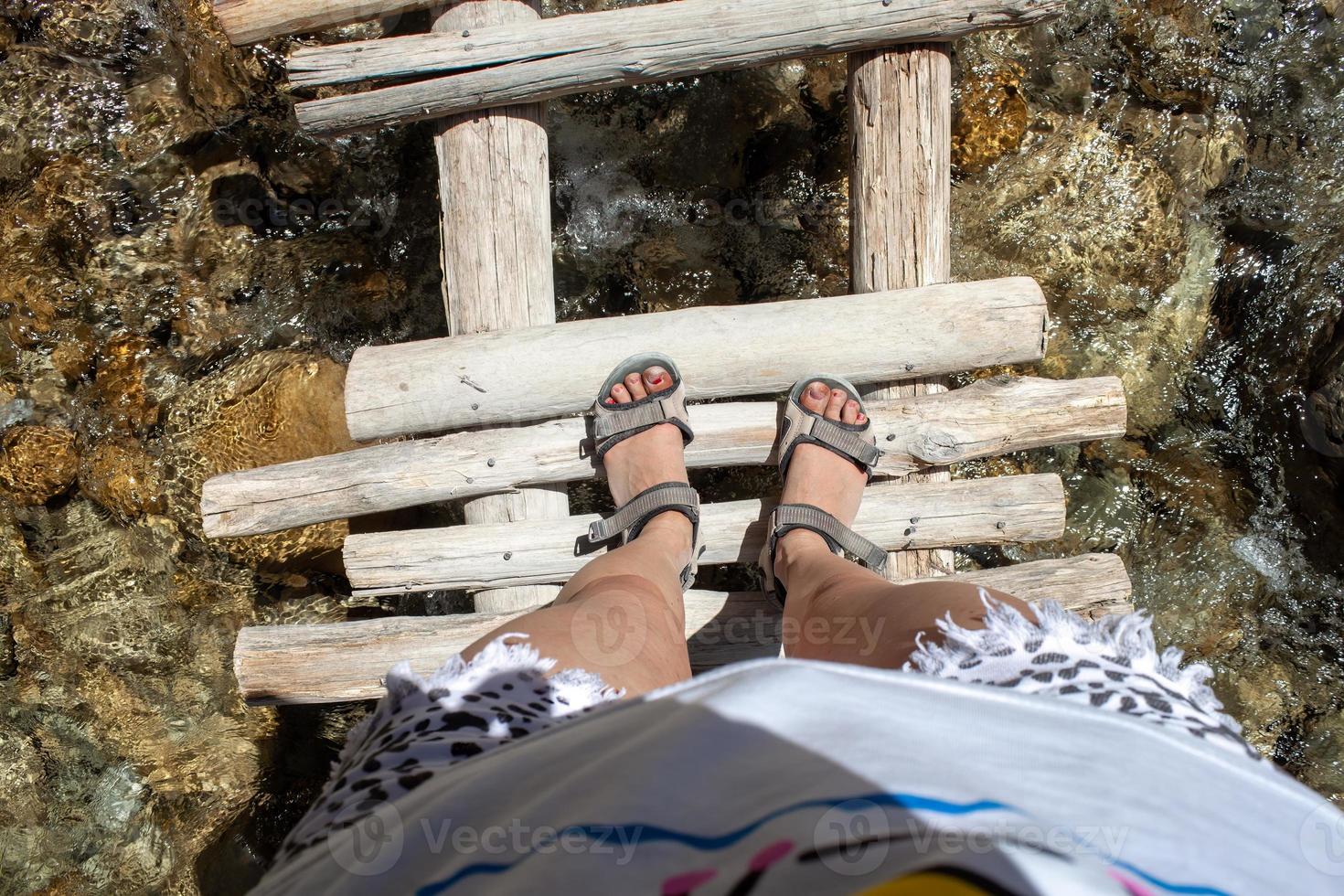 hermosa piernas de un viajero en un de madera puente por el río después un caminata en el montañas. viaje y libertad concepto foto