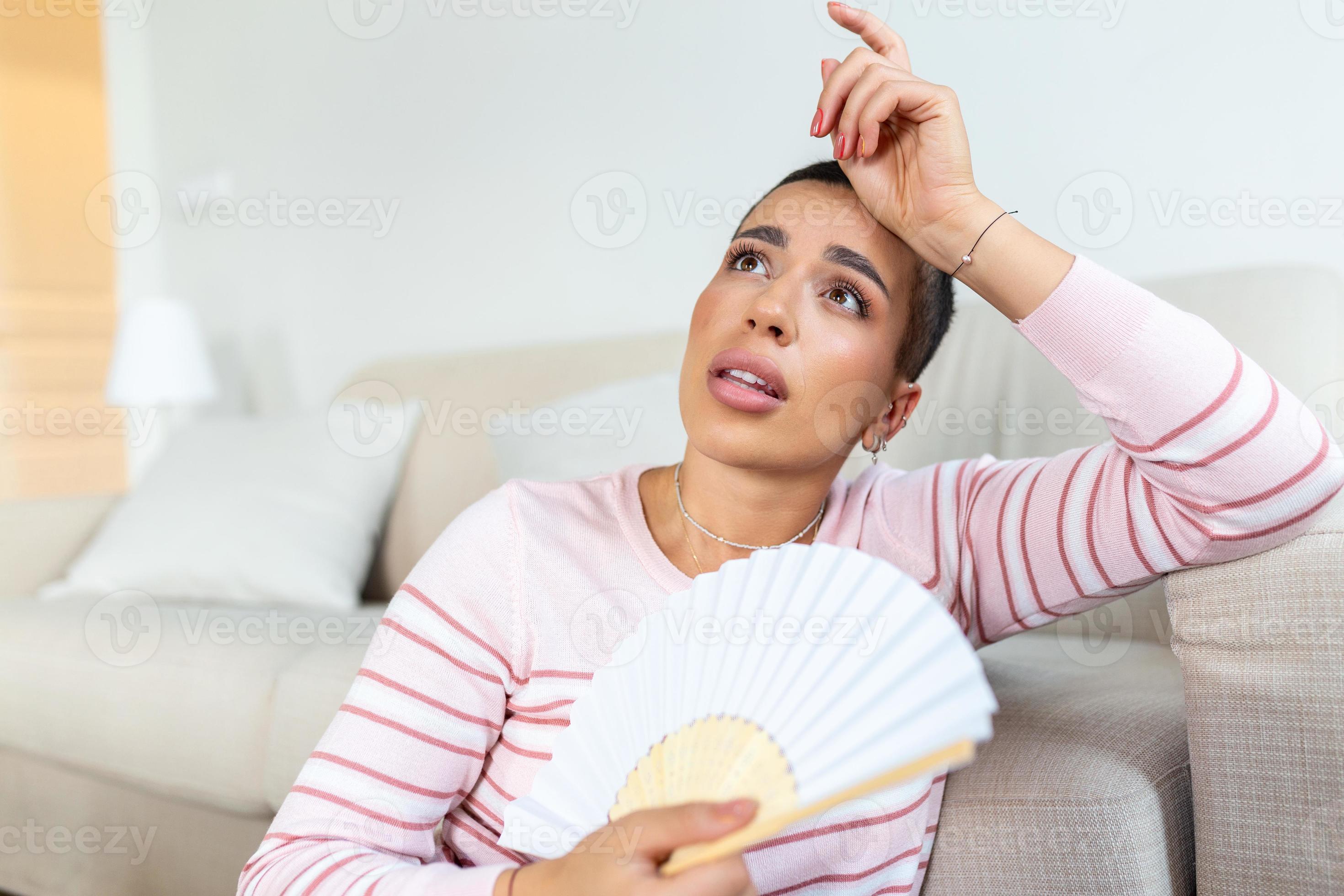 Overheated woman sit on couch at home feel warm waving with hand fan