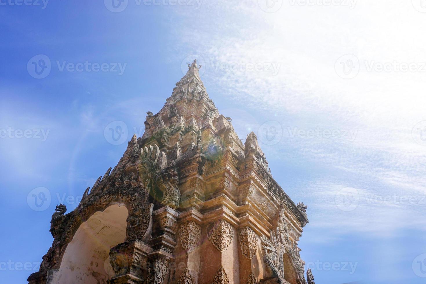 Look up view of traditional and ancient Thai Lanna art entrance gate of under bright blue sky with sun and lens flare background . photo