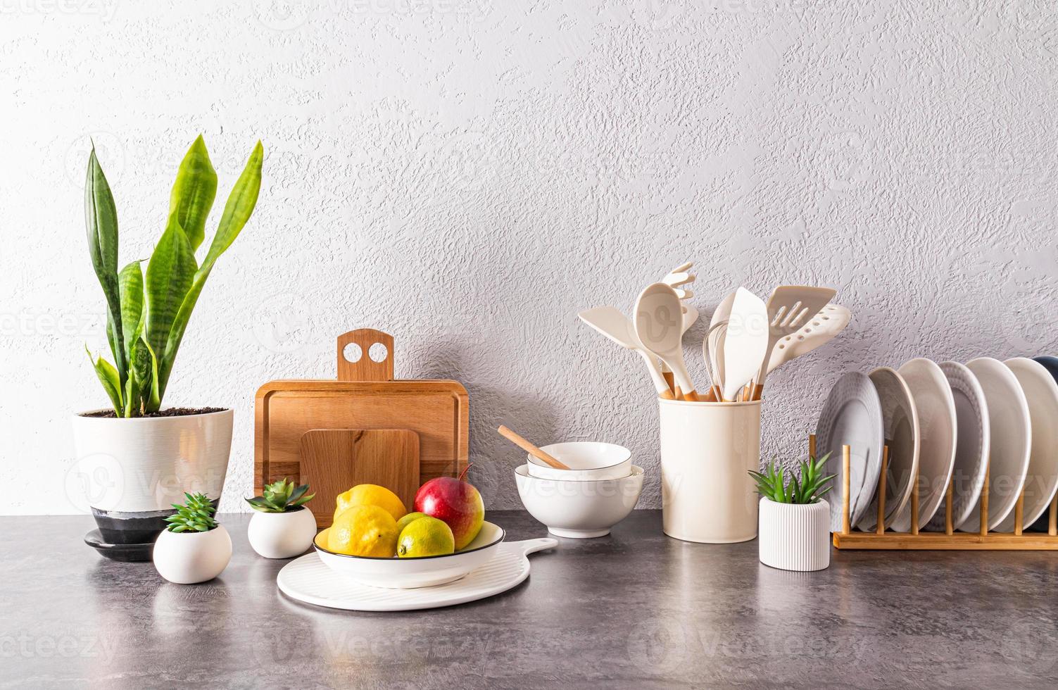 a set of various dishes, tools, a bowl of fruit on a stone countertop opposite a gray textured wall. space for text. still life. photo