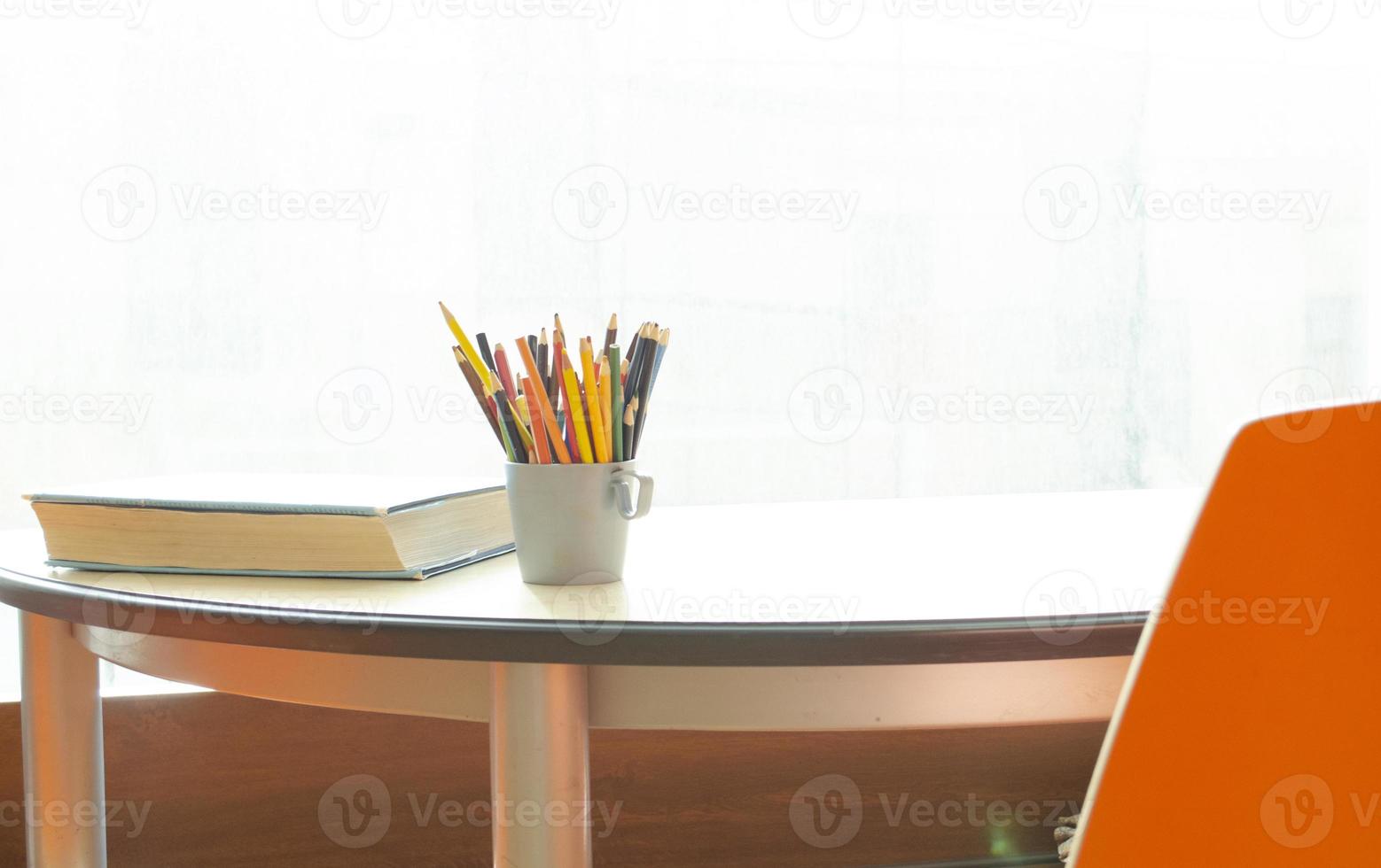 A cup with pencils and a corner of the book on the table by the window. Blurred background. Workplace for study. lightful room. photo