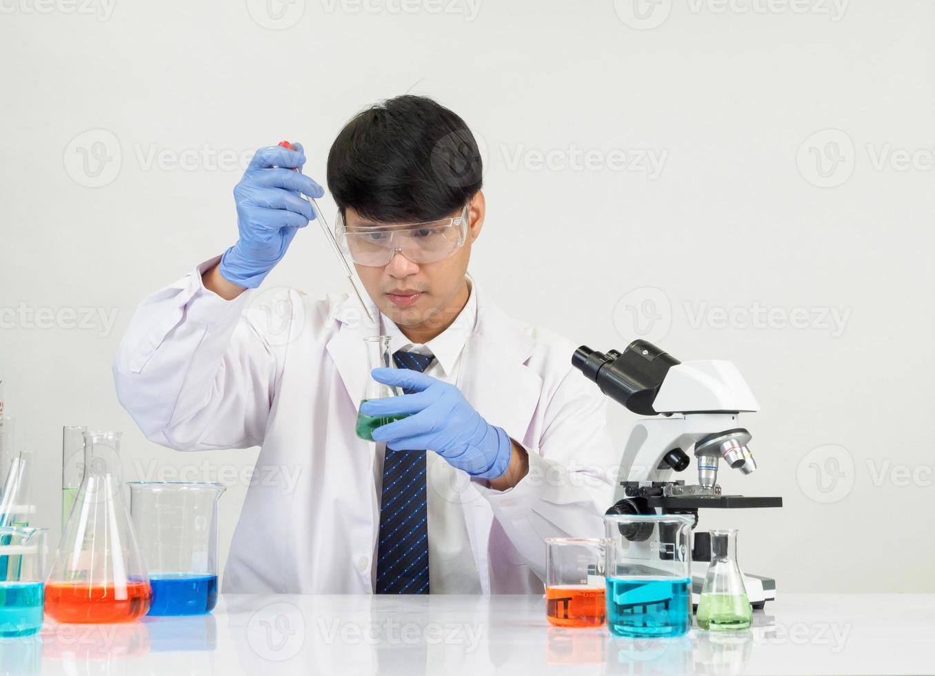 estudiante científico asiático en un laboratorio de mezcla de reactivos en un laboratorio de investigación científica con tubos de ensayo de varios tamaños y microscopios. sobre la mesa en el fondo blanco de laboratorio de química de laboratorio. foto