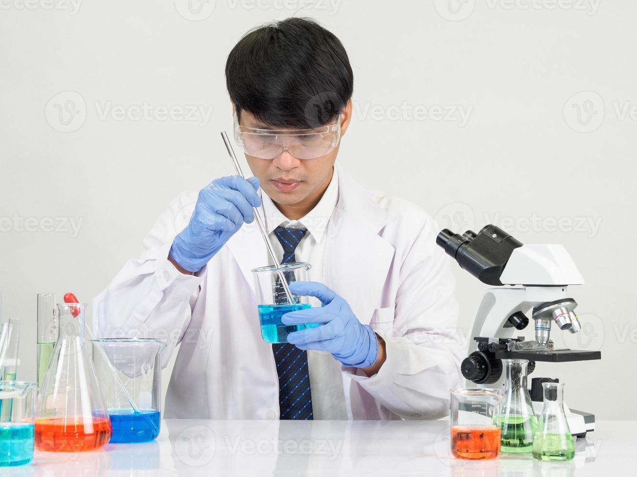 estudiante científico asiático en un laboratorio de mezcla de reactivos en un laboratorio de investigación científica con tubos de ensayo de varios tamaños y microscopios. sobre la mesa en el fondo blanco de laboratorio de química de laboratorio. foto