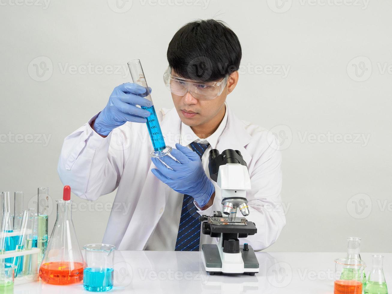 estudiante científico asiático en un laboratorio de mezcla de reactivos en un laboratorio de investigación científica con tubos de ensayo de varios tamaños y microscopios. sobre la mesa en el fondo blanco de laboratorio de química de laboratorio. foto