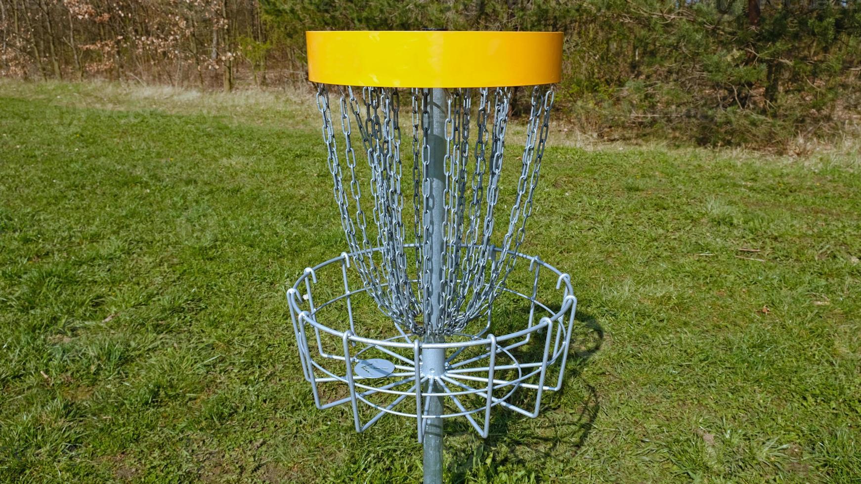 Disc Golf basket. Frisbee golf is sport and hobbie in outdoor park. Metal basket with chains for disc game surrounded by vibrant green trees. photo