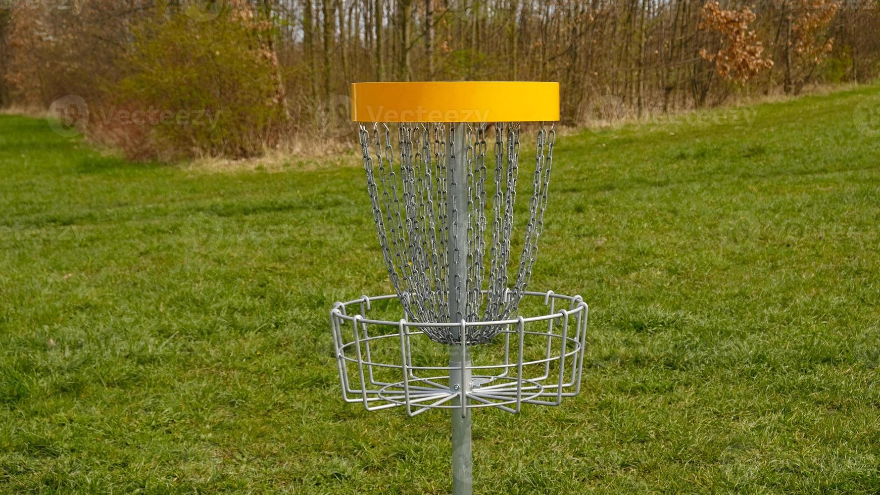 Disc Golf basket. Frisbee golf is sport and hobbie in outdoor park. Metal basket with chains for disc game surrounded by vibrant green trees. photo