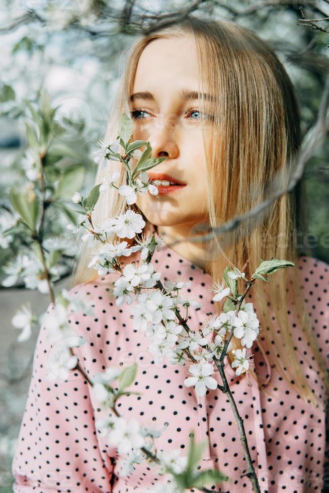 rubia niña en un primavera caminar en el jardín con Cereza flores hembra retrato, de cerca. un niña en un rosado polca punto vestido. foto