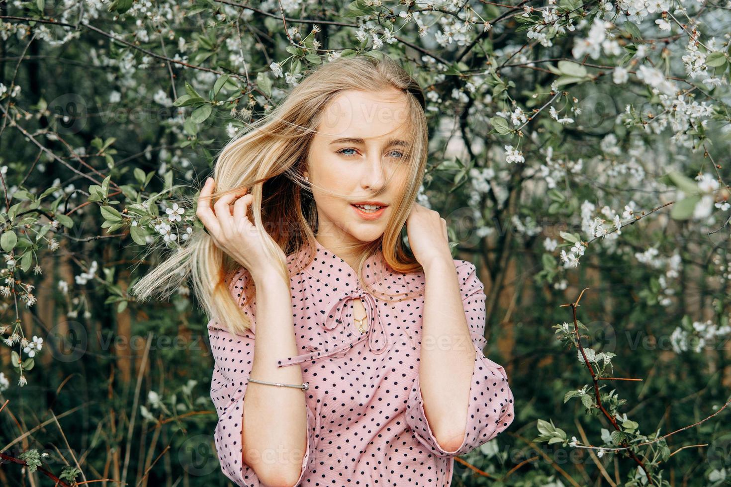 rubia niña en un primavera caminar en el jardín con Cereza flores hembra retrato, de cerca. un niña en un rosado polca punto vestido. foto