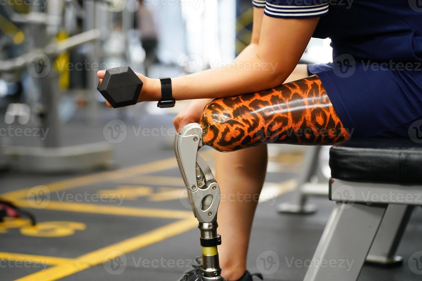 Young female with one prosthetic leg warms up by lifting light weights. Concept of living a woman's life with a prosthetic limb. photo