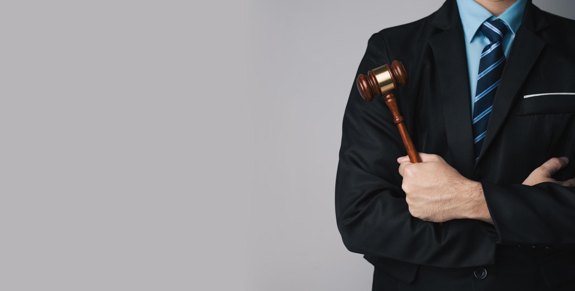 Law firm concept. Close up view of professional lawyer holding judge's hammer while standing against the grey wall. photo
