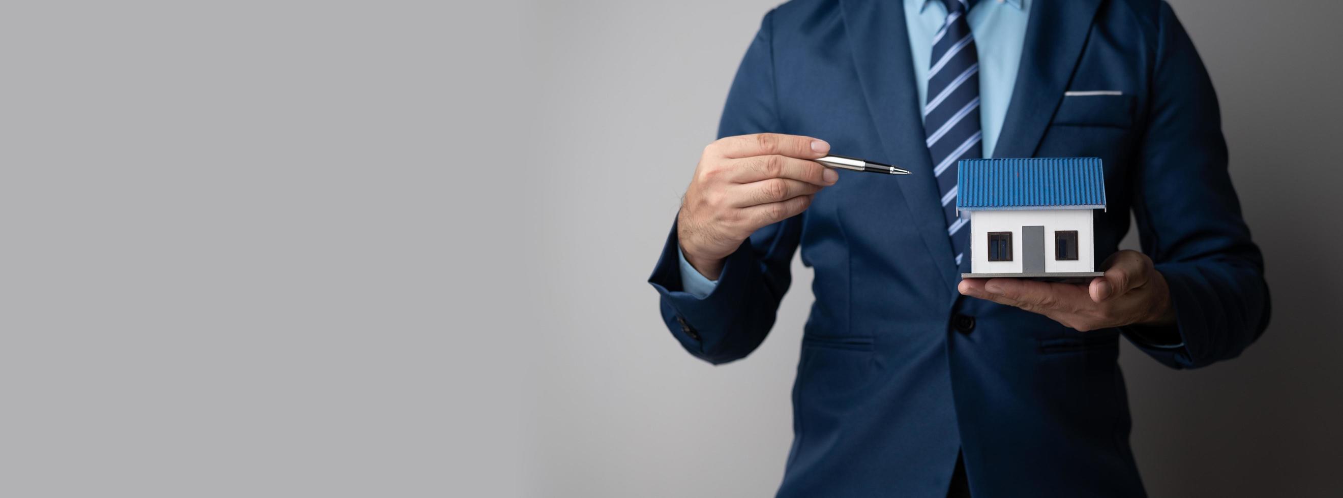 Close up view of young businessman or real estate agent holding a house model as a symbol of property investment. photo