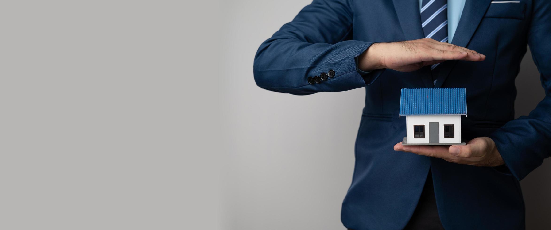 Close up view of young businessman or real estate agent holding a house model as a symbol of property investment. photo