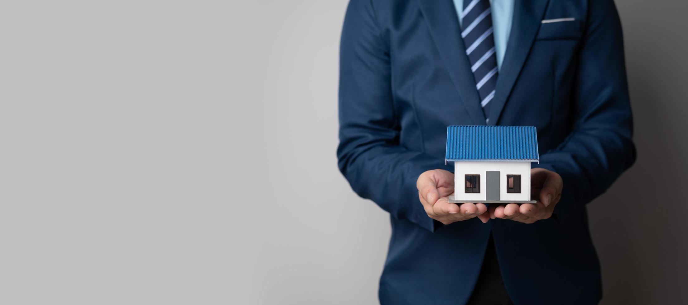 Close up view of young businessman or real estate agent holding a house model as a symbol of property investment. photo