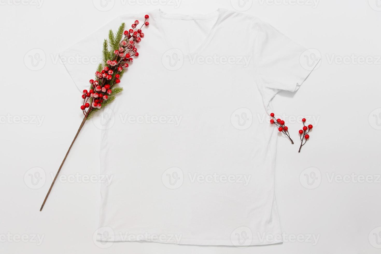 Close up white blank template t shirt with copy space and Christmas Holiday concept. Top view mockup t-shirt and red holidays decorations on white background. Happy New Year accessories. Xmas outfit photo
