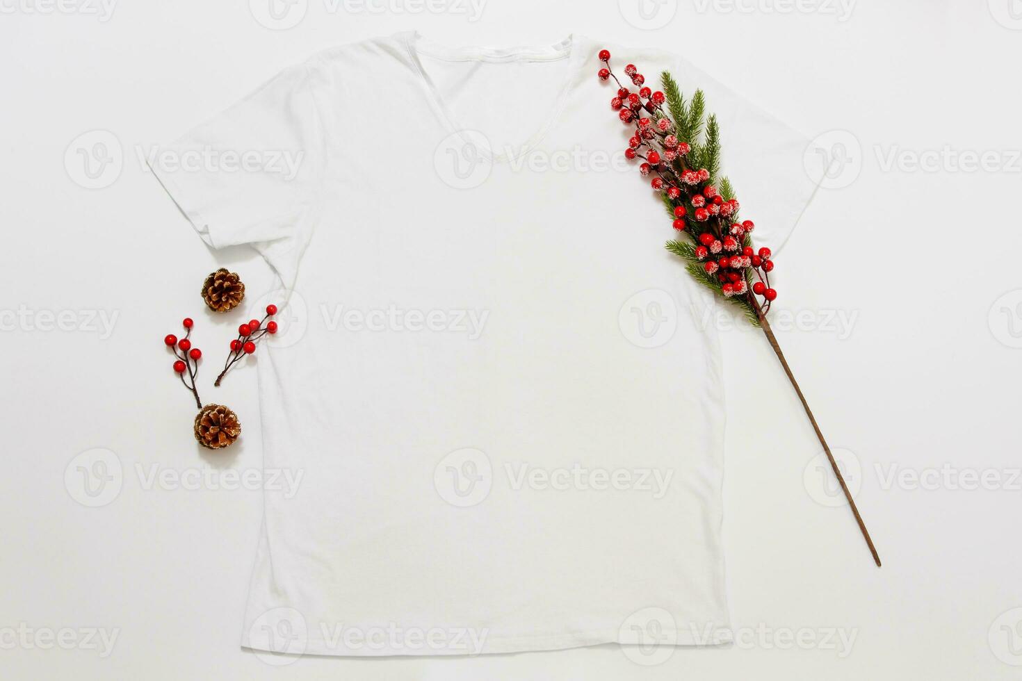 Close up white blank template t shirt with copy space and Christmas Holiday concept. Top view mockup t-shirt and red holidays decorations on white background. Happy New Year accessories. Xmas outfit photo