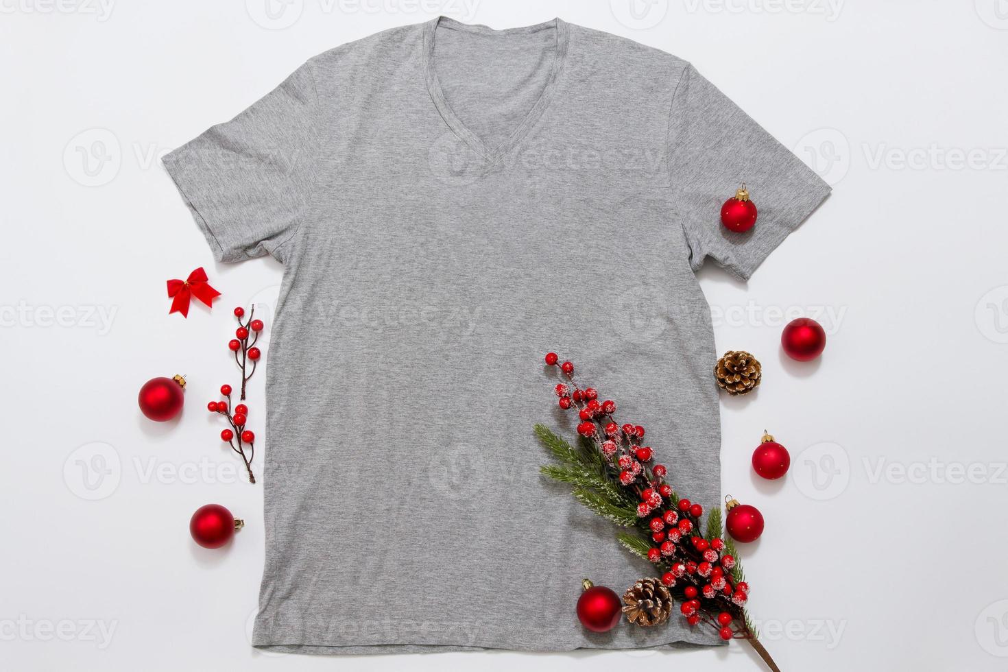 Close up grey blank template t shirt with copy space and Christmas Holiday concept. Top view mockup t-shirt and red holidays decorations on white background. Happy New Year accessories. Xmas outfit photo